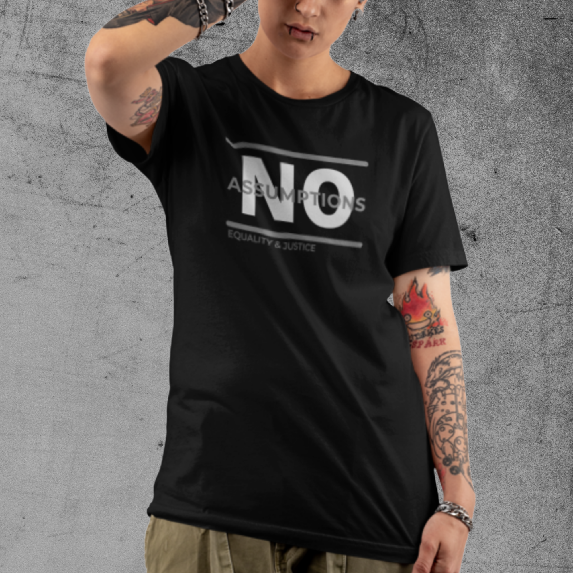 A non-binary model is wearing a unisex, crew-neck style t-shirt in solid black. Bold "NO Assumptions" brand graphic on the front, including the tag phrase “Equality & Justice” on lower left corner of the logo.