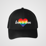 A black unisex snapback trucker hat featuring a bold rainbow heart design on the front. The heart is filled with horizontal rainbow stripes, and the words "love is love" are written in elegant white script across it, symbolizing support for LGBTQIA2S+ equality and inclusivity.