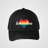 A black unisex snapback trucker hat featuring a bold rainbow heart design on the front. The heart is filled with horizontal rainbow stripes, and the words "love is love" are written in elegant white script across it, symbolizing support for LGBTQIA2S+ equality and inclusivity.