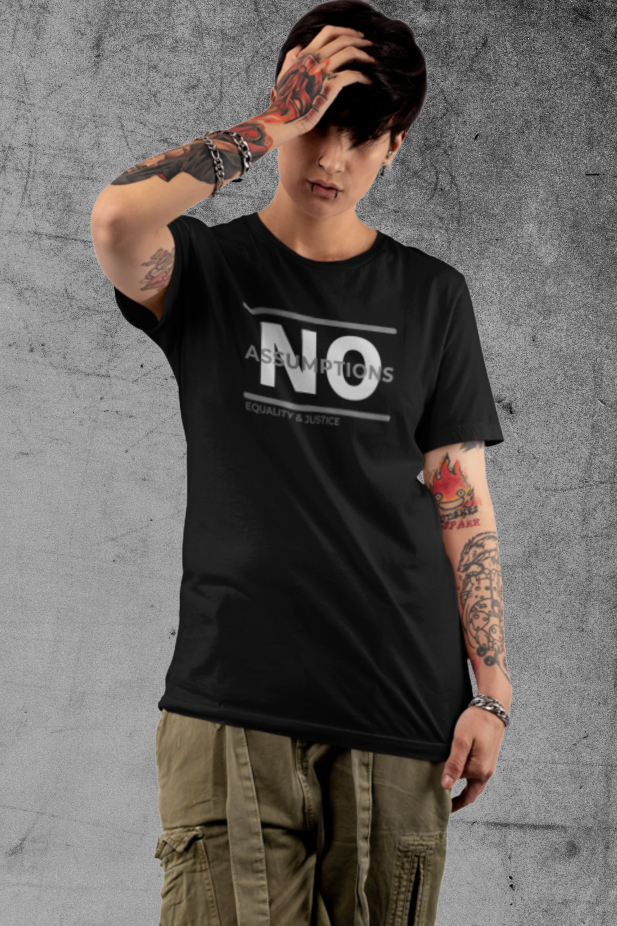 A non-binary model is wearing a unisex, crew-neck style t-shirt in solid black. Bold "NO Assumptions" brand graphic on the front, including the tag phrase “Equality & Justice” on lower left corner of the logo. 